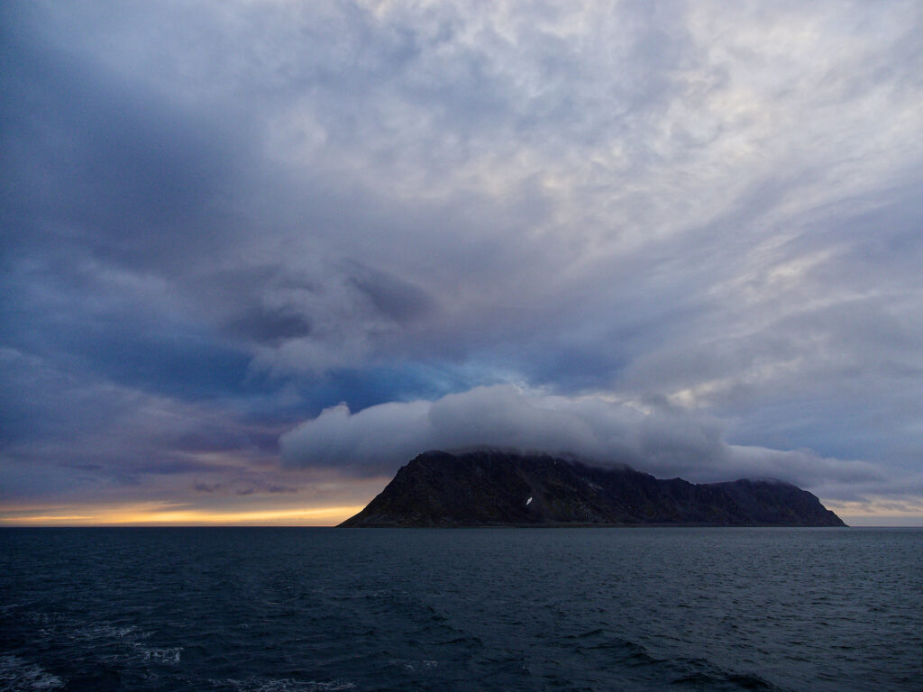 Svalbard: Fuglefjorden-Landschaft mit Meer, Insel und bewölktem Himmel.