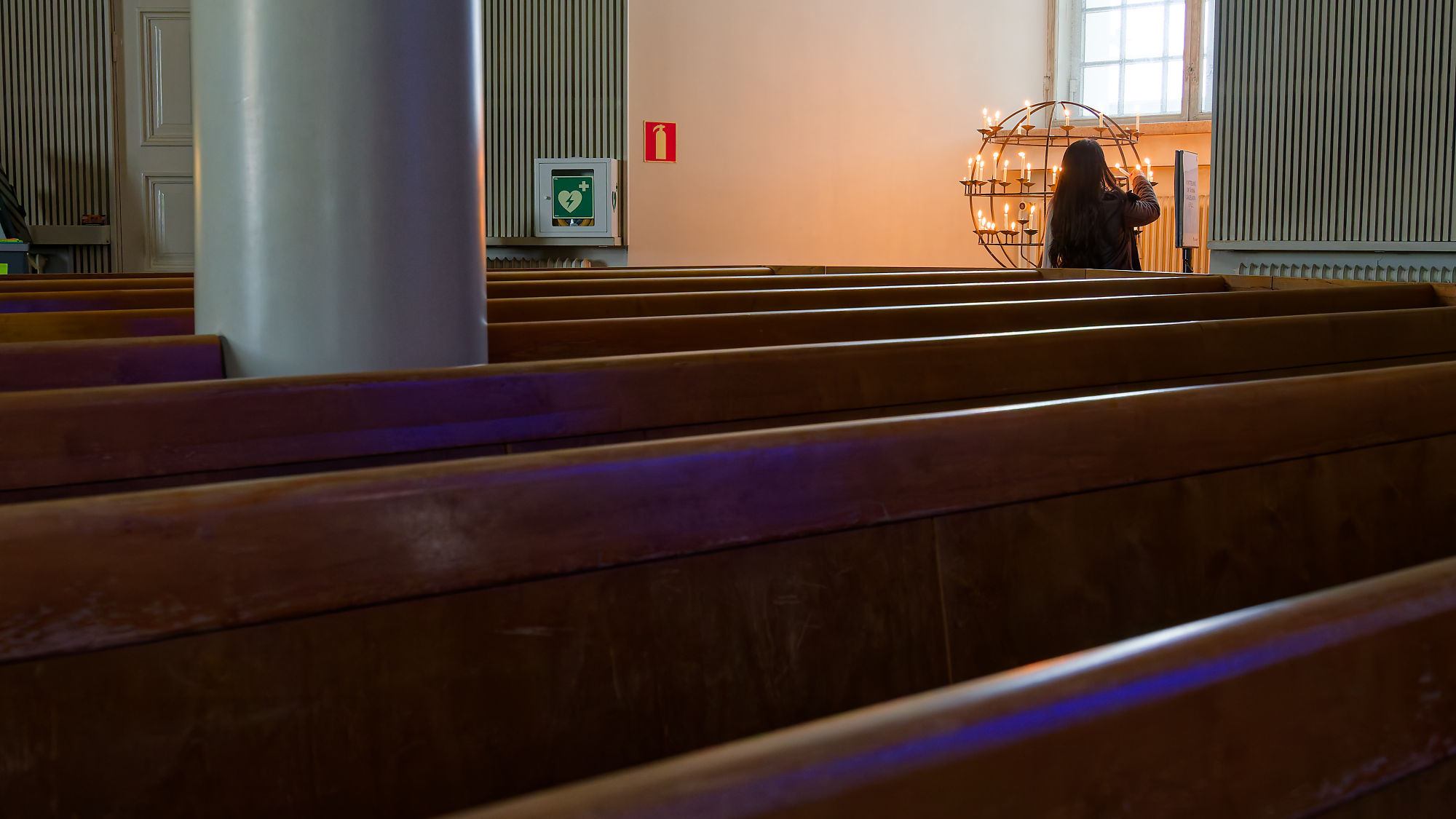 Andacht in Helsinki: Frau zündet Kerze in Kirche an. Gebetsbank im Vordergrund.