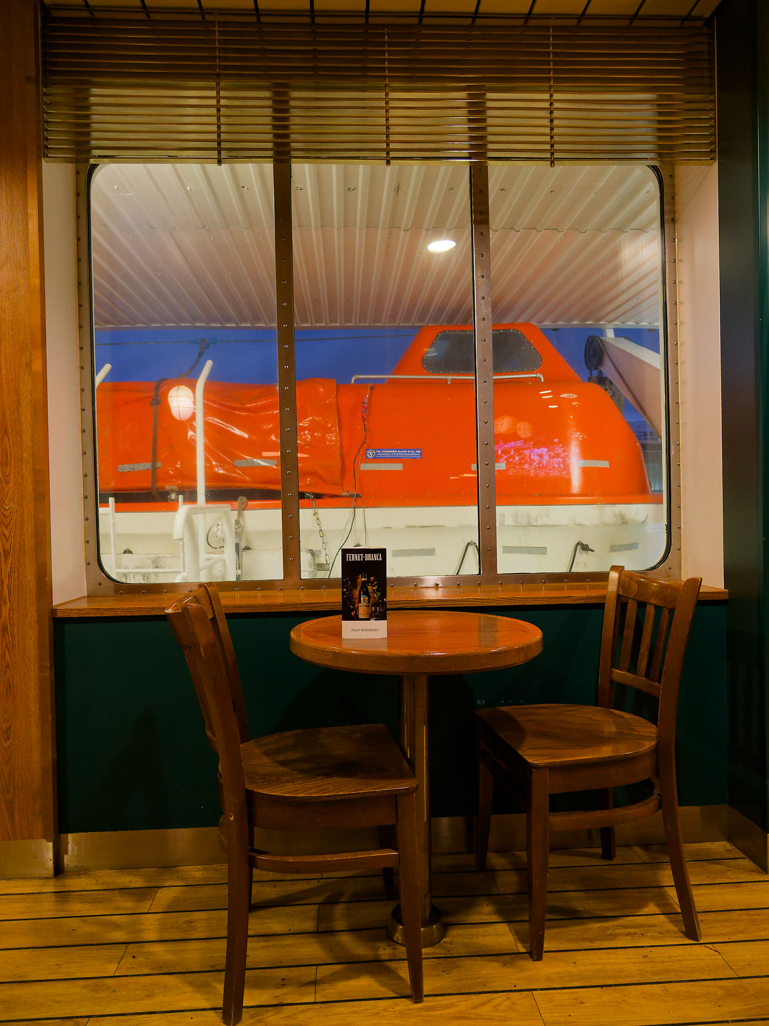 Tisch mit Stühlen auf einer Helsinki Fähre, Blick auf Rettungsboot durch Fenster. Finnland Reise.