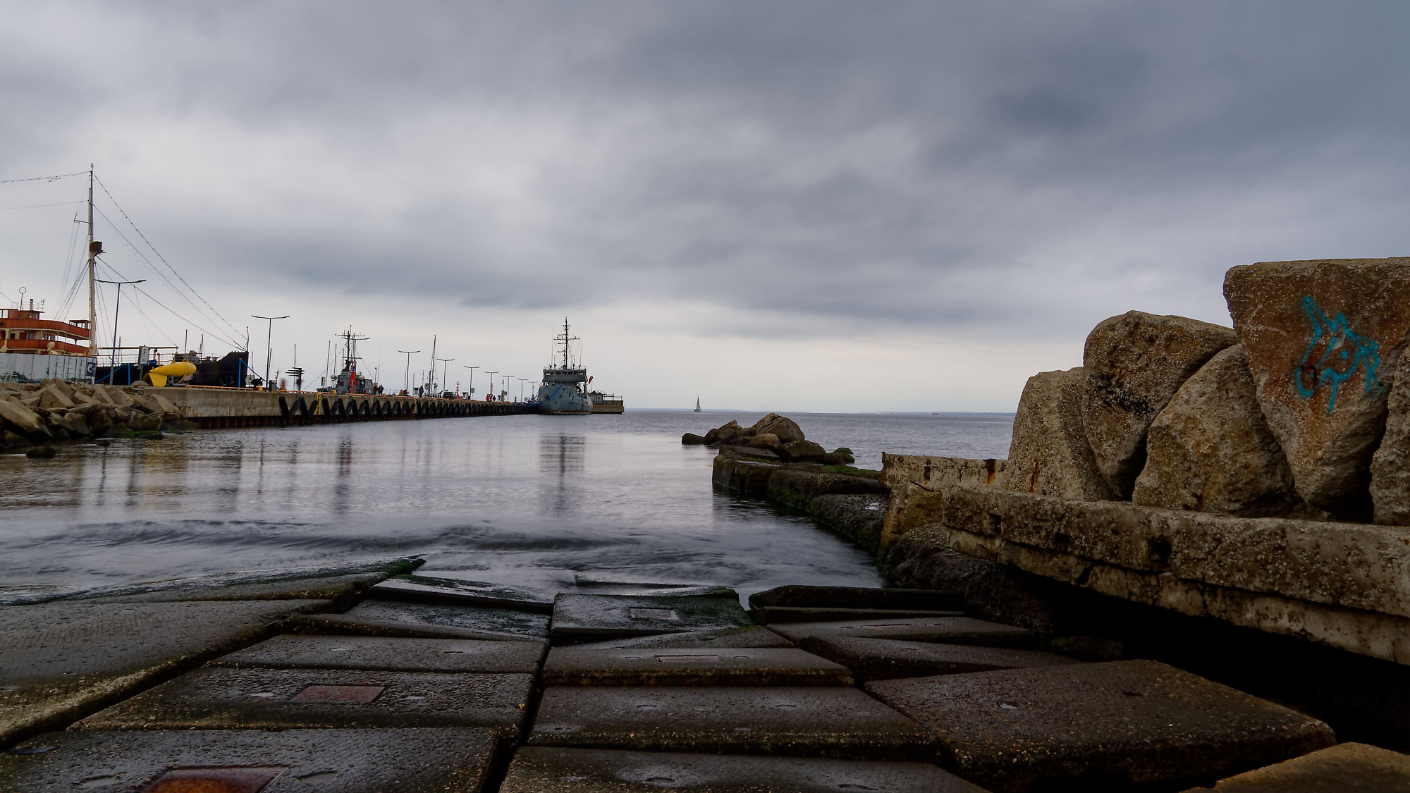 Tallinn Hafen, Estland. Schiffe am Kai unter bewölktem Himmel. Steine im Vordergrund.