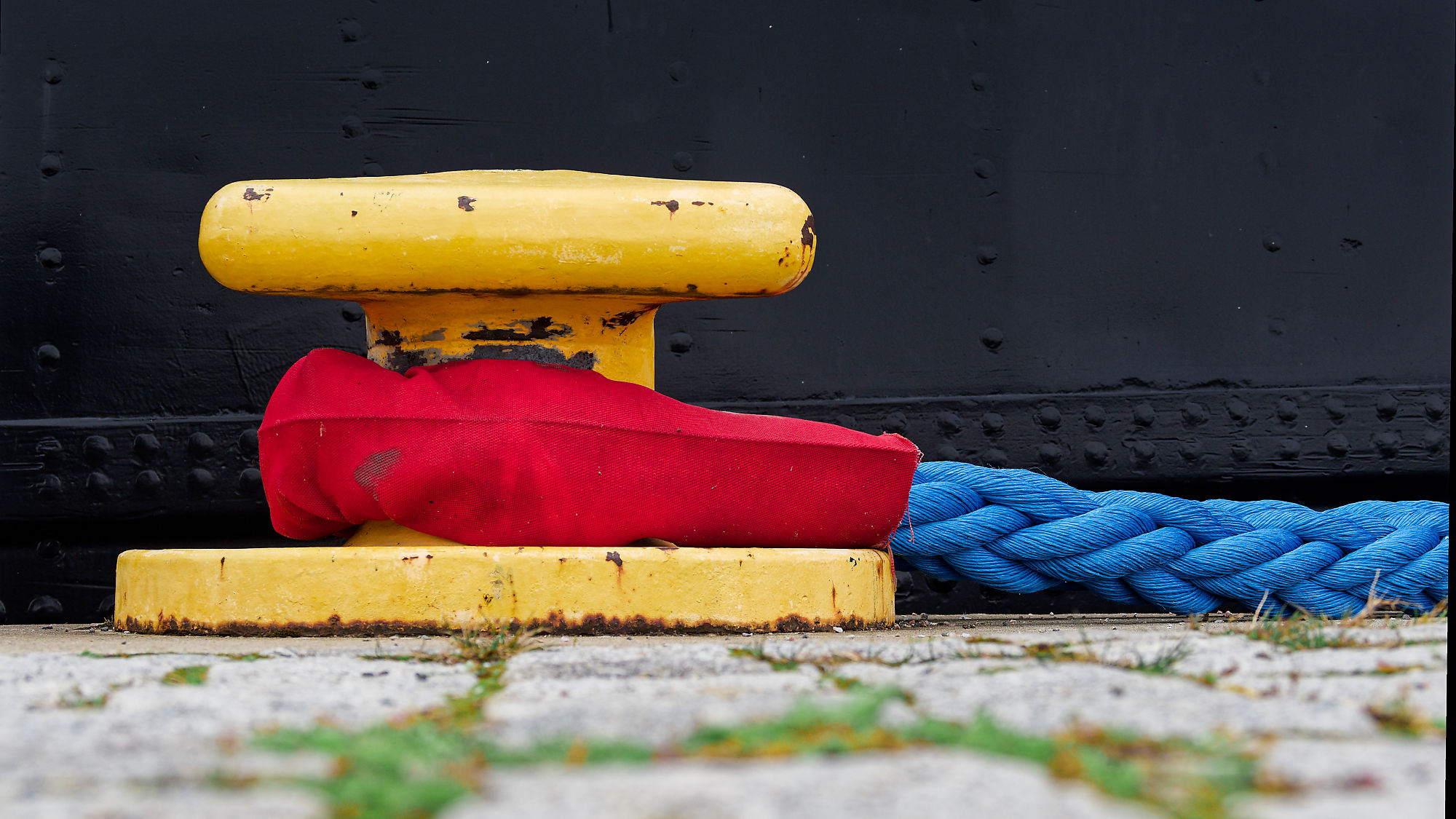 Gelber Poller mit rotem Schutz und blauem Seil am Hafen in Tallinn.