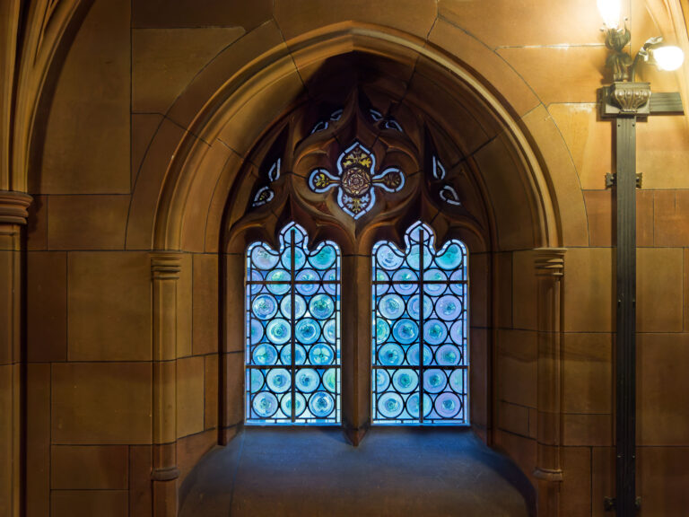 Manchester: Gotisches Fenster mit blauem Glas und dekorativen Mustern in historischer Architektur.