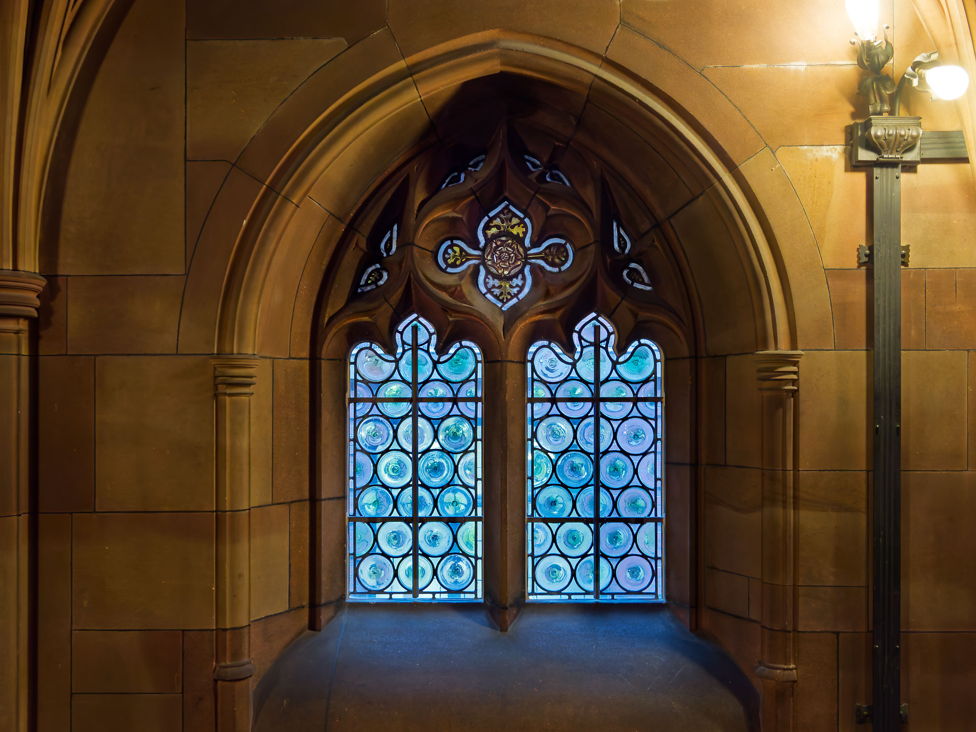 Manchester Manchester: Gotisches Fenster mit blauem Glas und dekorativen Mustern in historischer Architektur.