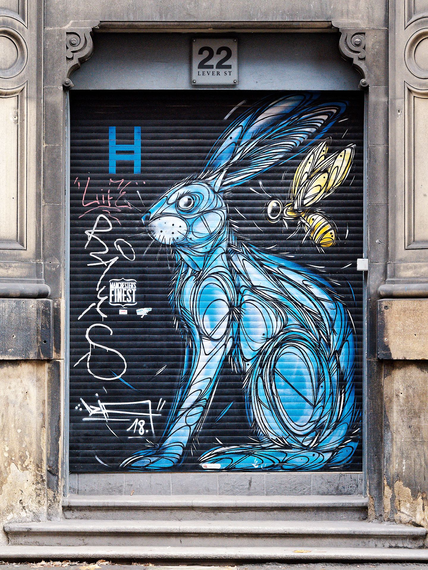 Manchester Manchester Streetart: Blauer Hase mit Biene an Rolltor, Lever Street 22. Urbane Kunstszene, Wandmalerei.