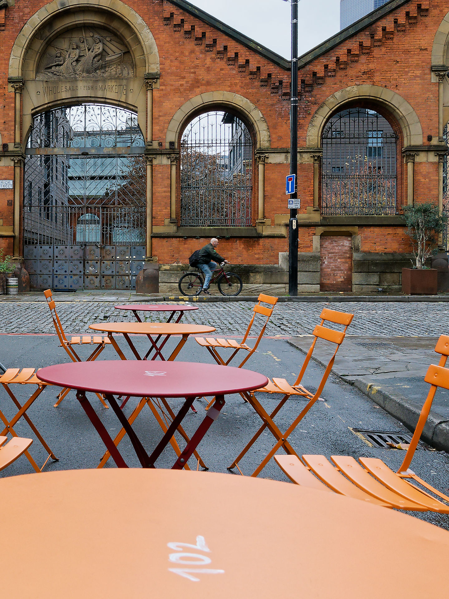 Manchester Außenansicht des Wholesale Fish Market in Manchester mit einem Radfahrer und Tischen im Vordergrund.