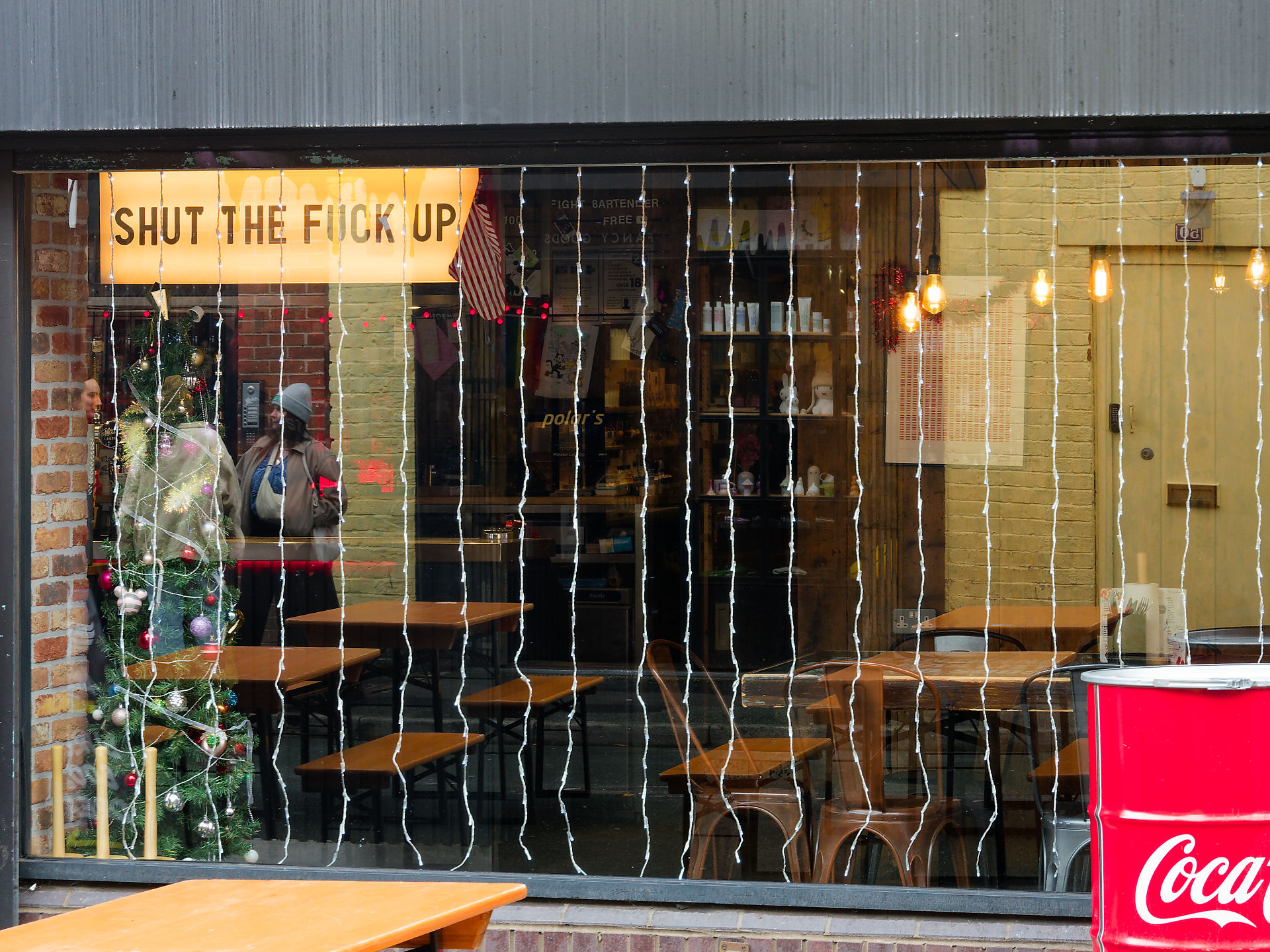 Manchester Manchester restaurant window with Christmas tree, lights, and a sign reading "Shut the F*ck Up"