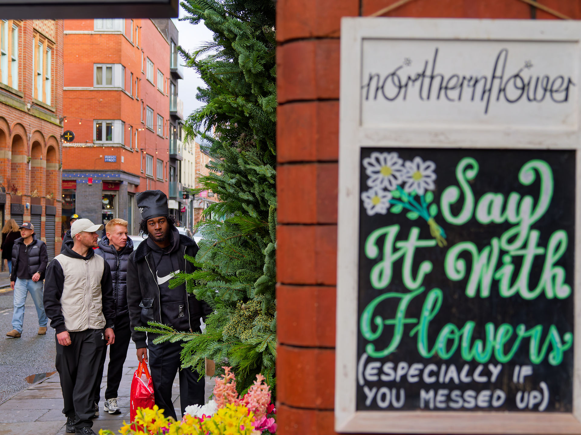 Manchester Männer in Manchester gehen an einem Blumenladen vorbei, "Sag es mit Blumen" Schild.