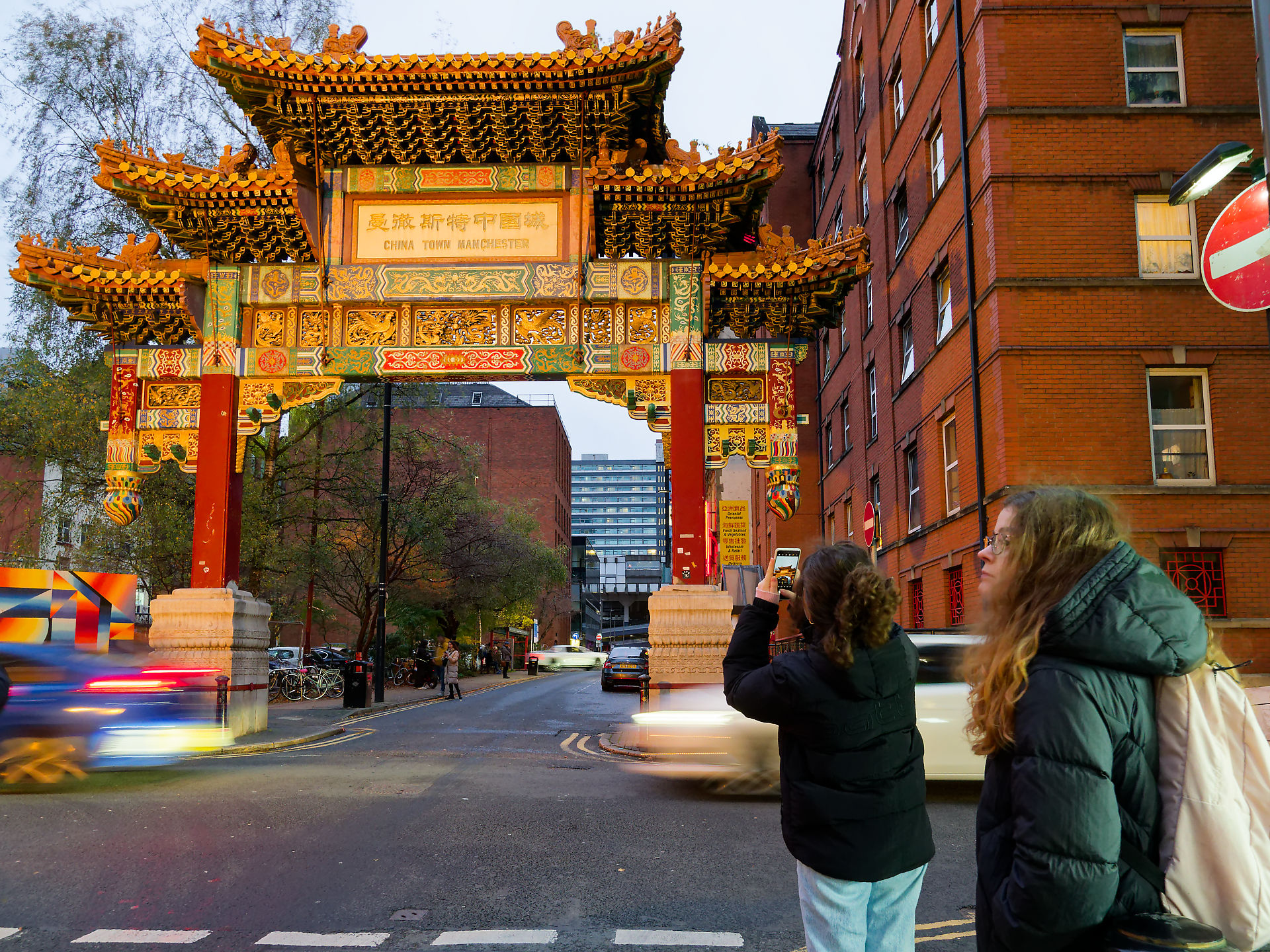Manchester Chinatown Manchester Torbogen: Touristinnen fotografieren das Wahrzeichen. Beleuchtetes Tor am Abend in Manchester.
