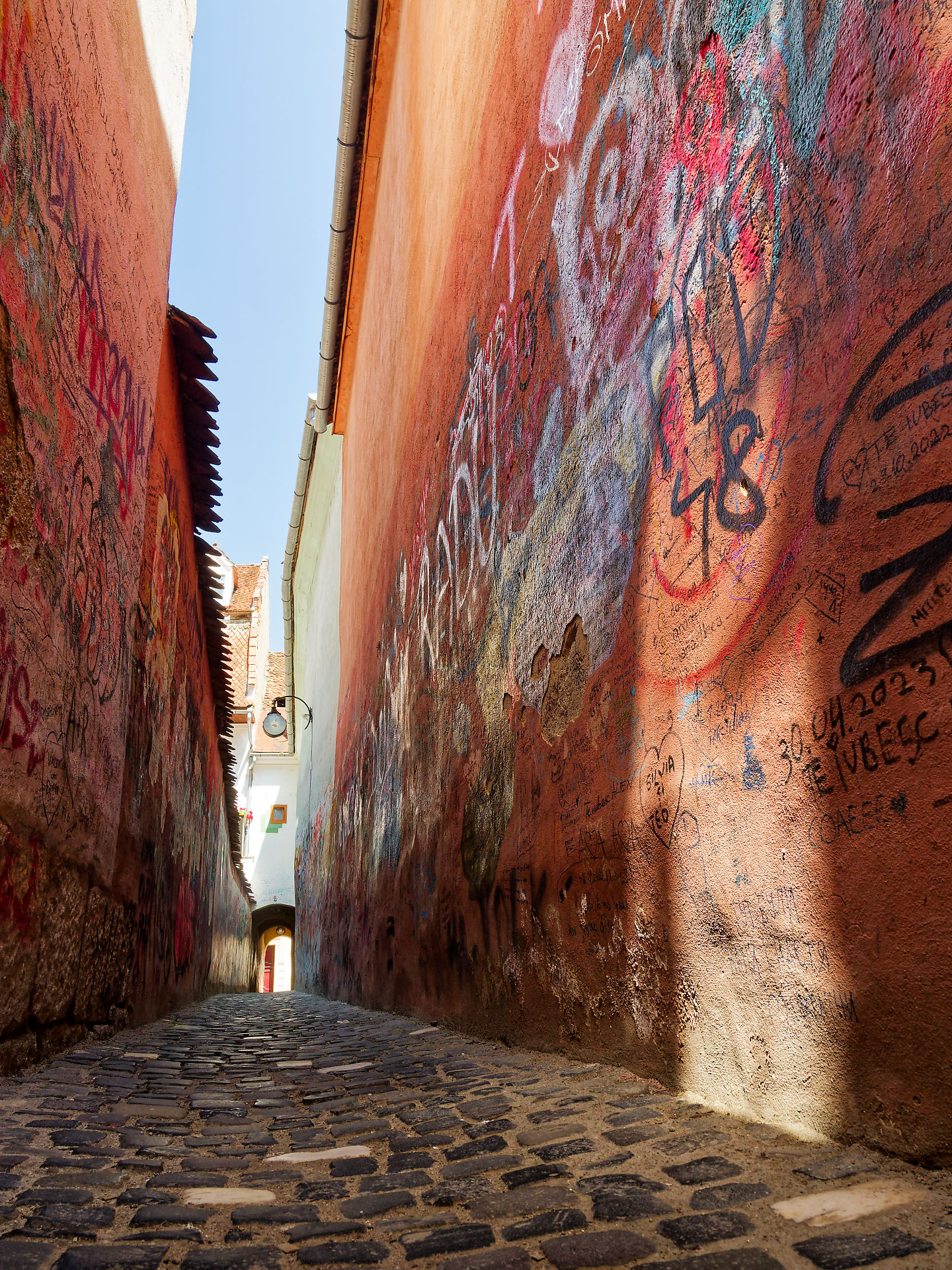 Schmale Gasse in Brasov, Rumänien. Pflastersteine, Graffiti an roten Mauern. Mittelalterliche Architektur.