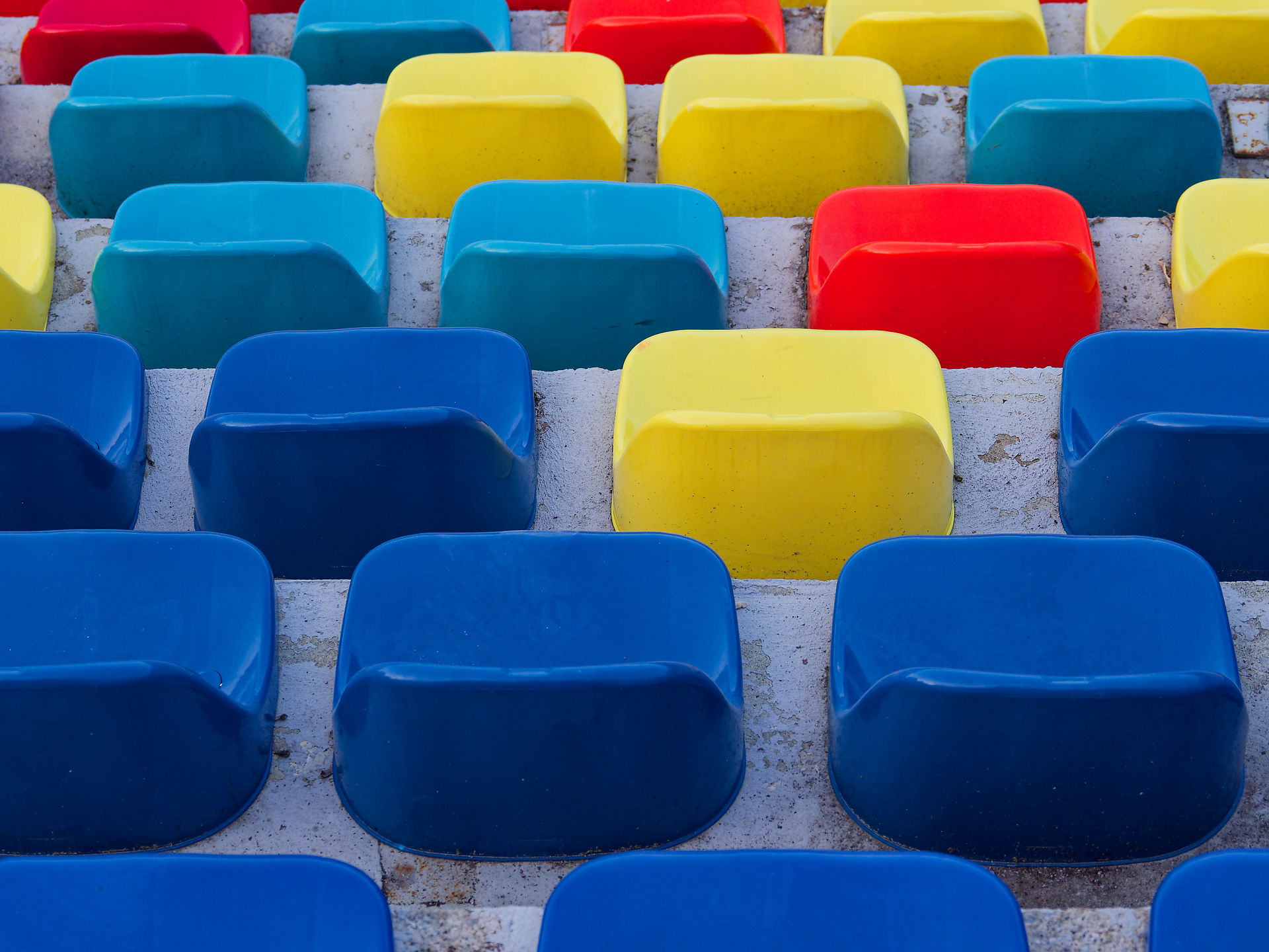 Farbenfrohe Stadionsitze in Blau, Gelb und Rot. Arena-Bestuhlung, Zuschauerplätze.