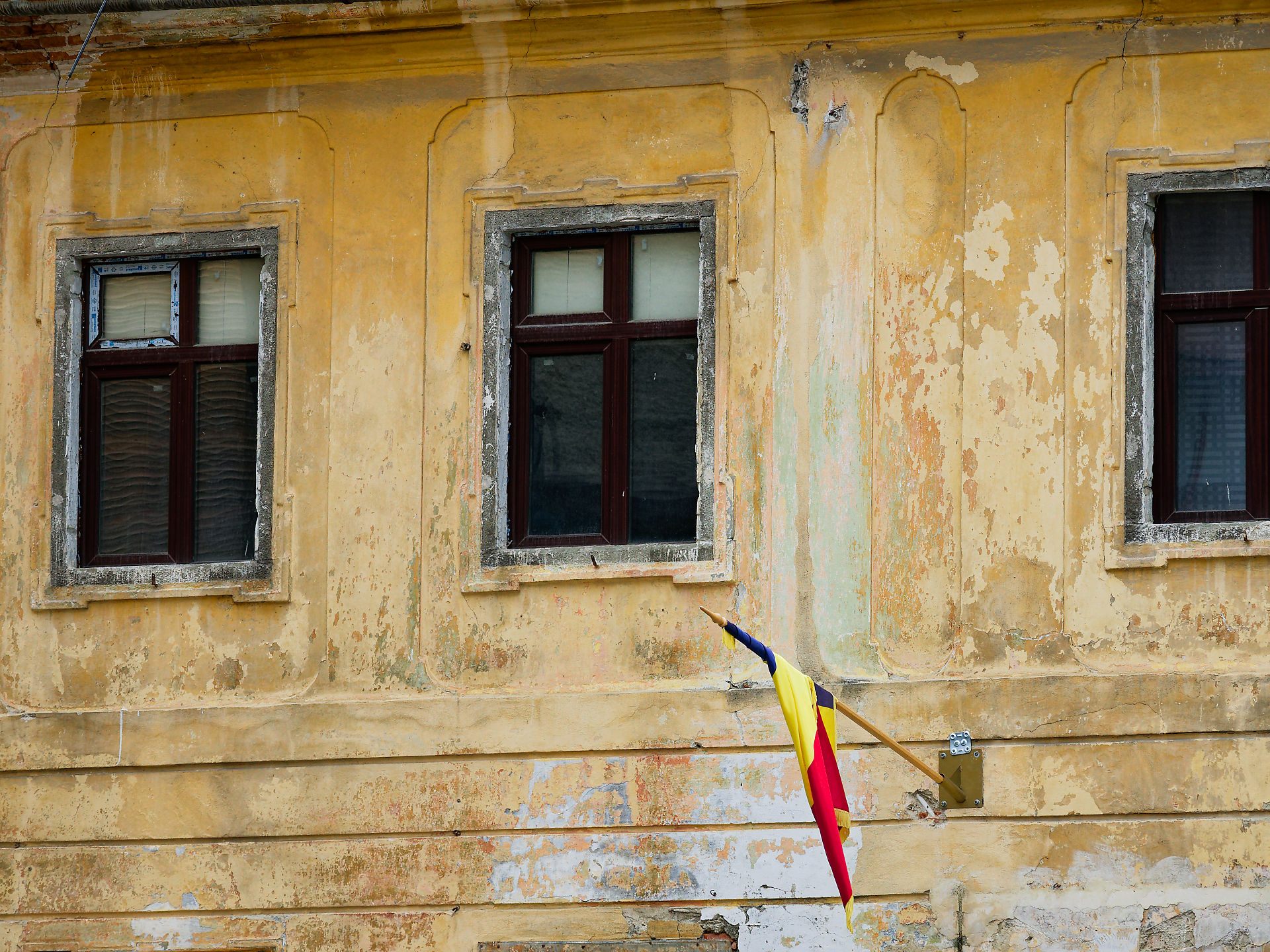 Gelbe Fassade in Brasov, Rumänien, mit Fenstern und rumänischer Flagge. Architektur und Kultur.