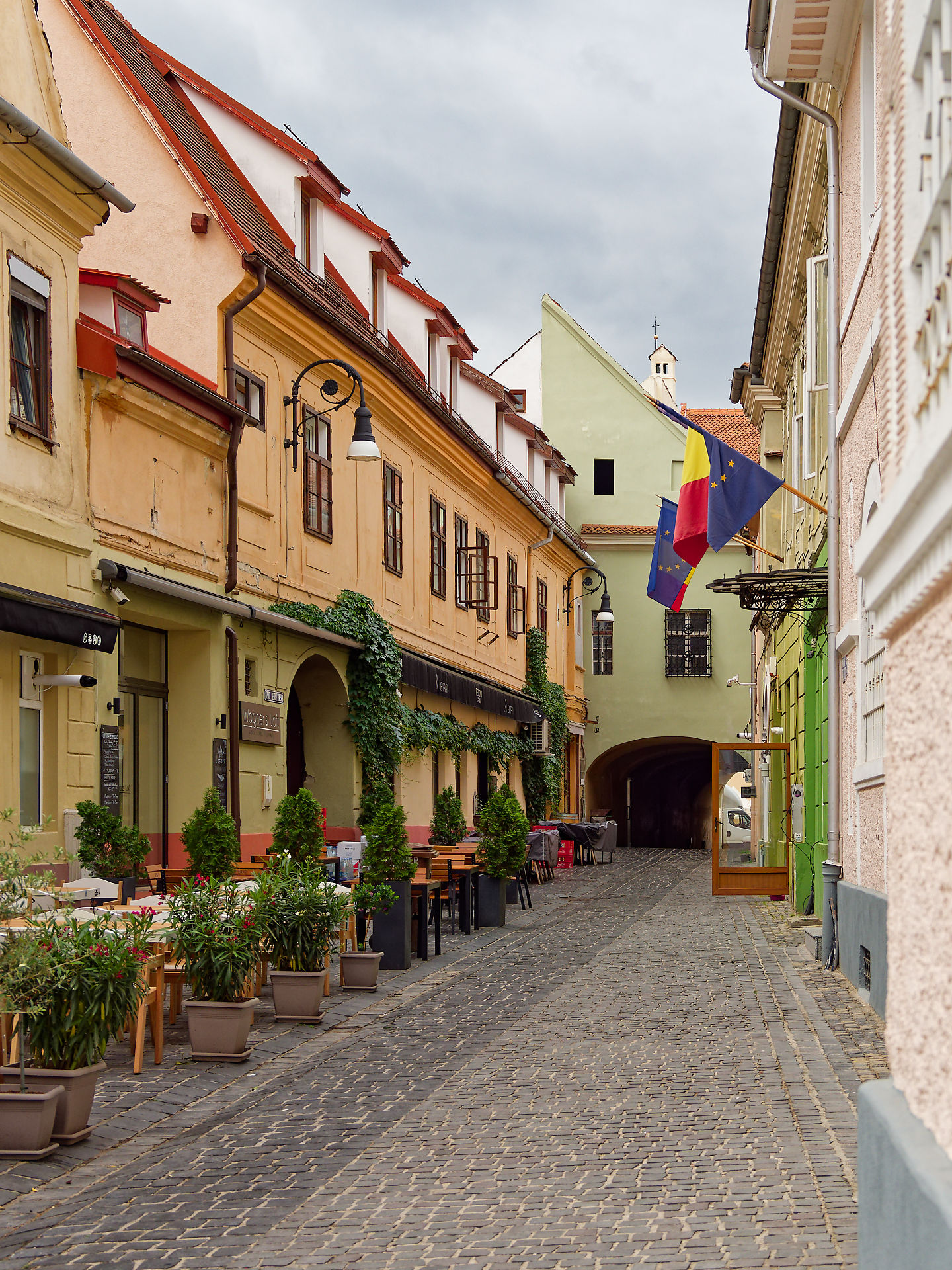 Brasov, Rumänien: Kopfsteinpflasterstraße mit Cafés und Flaggen. Architektur in der Altstadt.