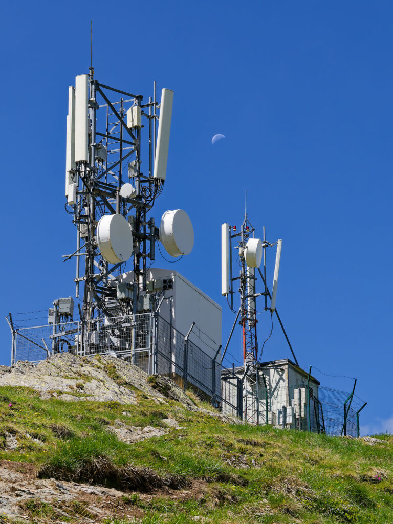 Mobilfunkmast in Rumänien unter blauem Himmel. Antennen und Telekommunikation auf Berg. Abnehmender Mond am Himmel