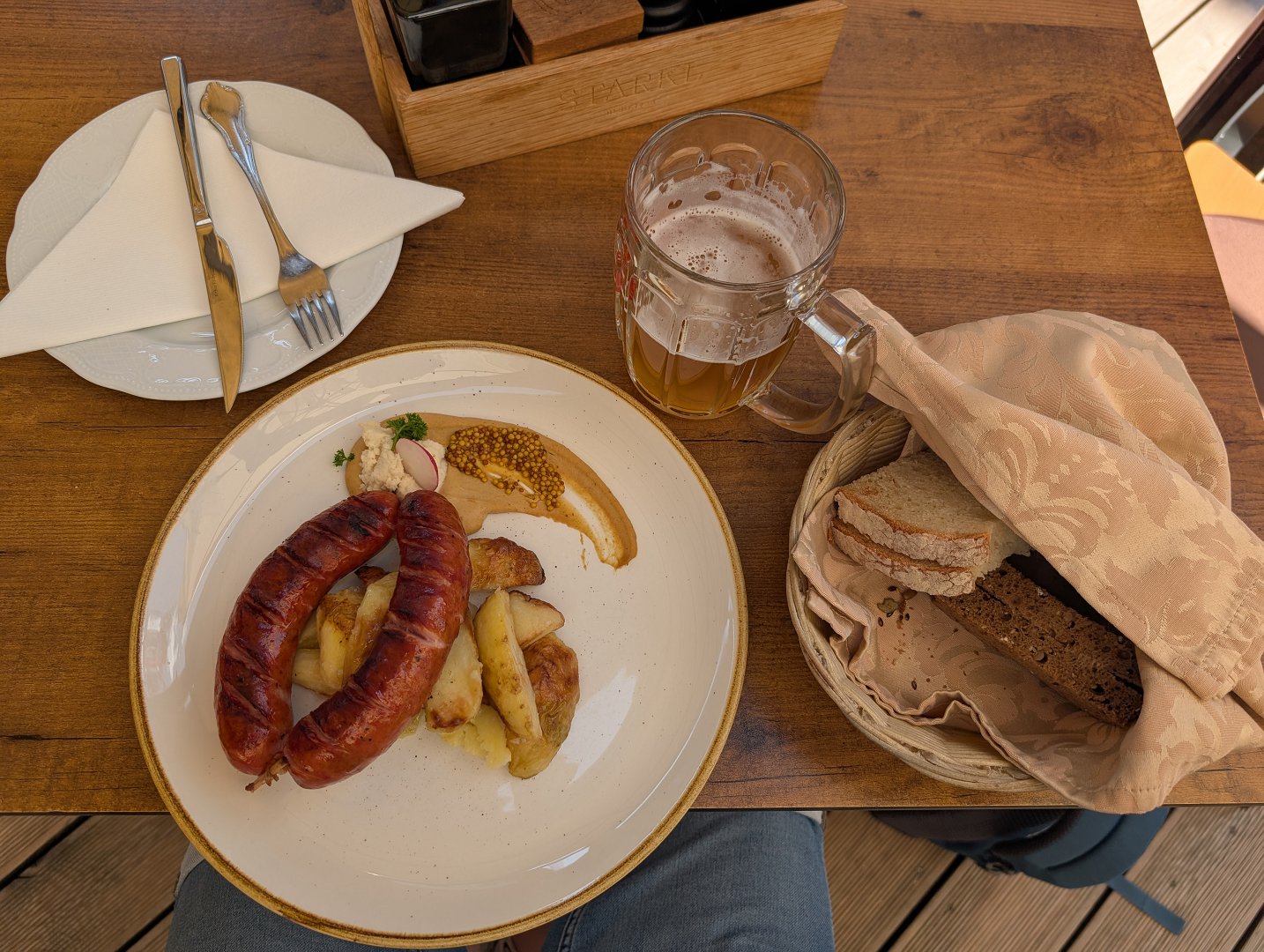 Krainer Wurst mit Beilage, Bier und Brot auf einem Tisch im Restaurant Starkl in Bled.