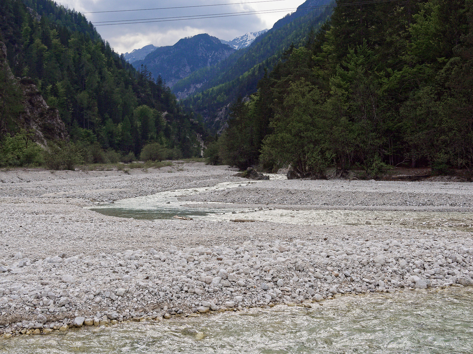 Soca Fluss in Slowenien. Flussbett mit Steinen, Berge und Wald im Hintergrund.