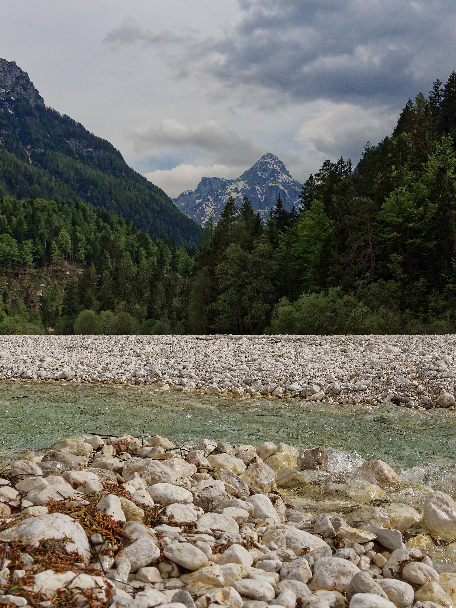 Soca Fluss, Slowenien: Türkisblaues Wasser, Steine, Berge und Wald unter bewölktem Himmel. Natur pur!