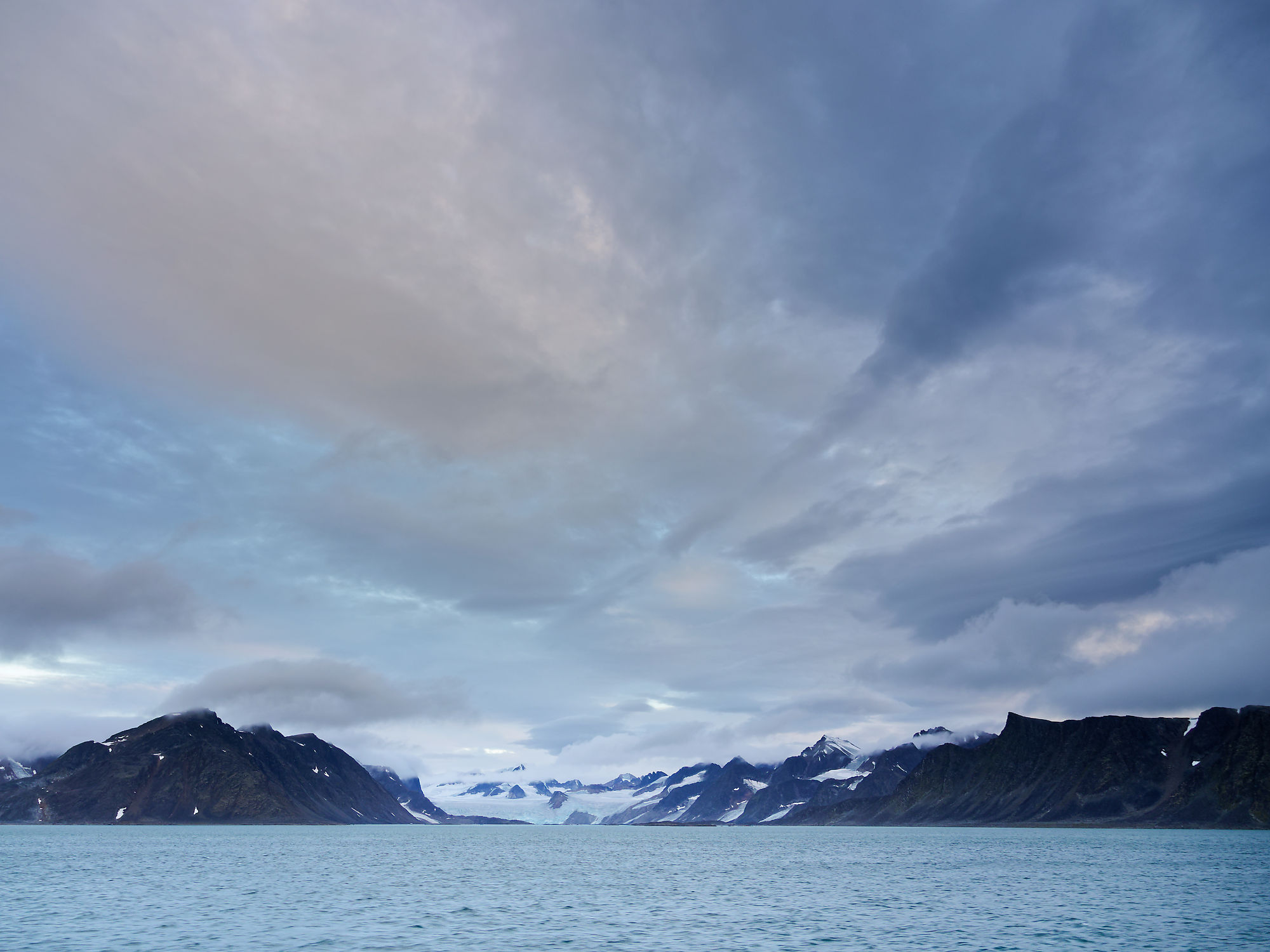 Fuglefjorden, Spitzbergen: Arktische Landschaft mit Bergen, Gletscher und bewölktem Himmel über dem Meer.