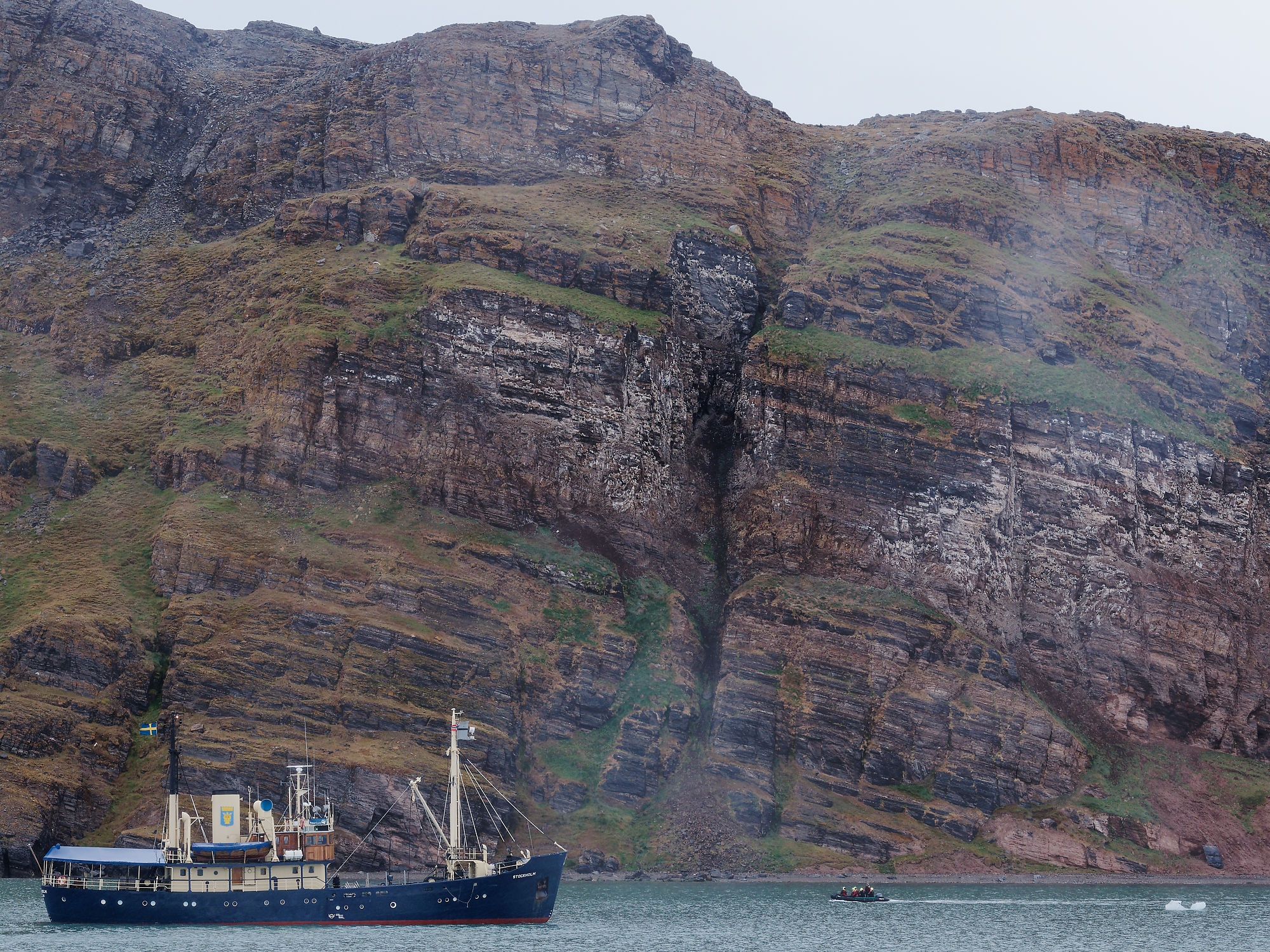 Kongsfjorden, Spitzbergen: Schiff vor Felswand. Arktische Landschaft mit Boot und steiler Küste. Naturerlebnis in Norwegen.