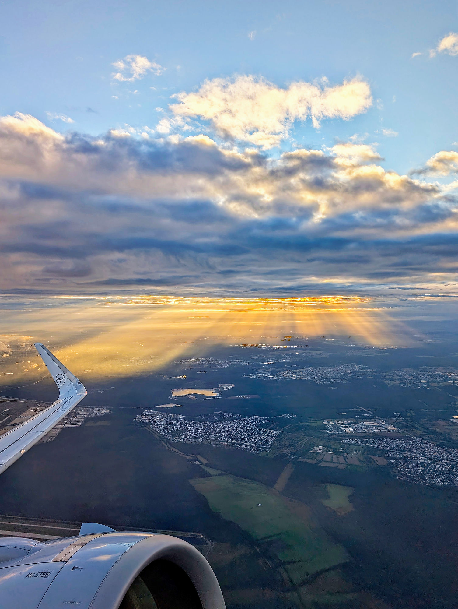 Flugzeugblick auf Frankfurt: Sonnenstrahlen durchbrechen Wolken über Stadt. Flugreise-Impression.