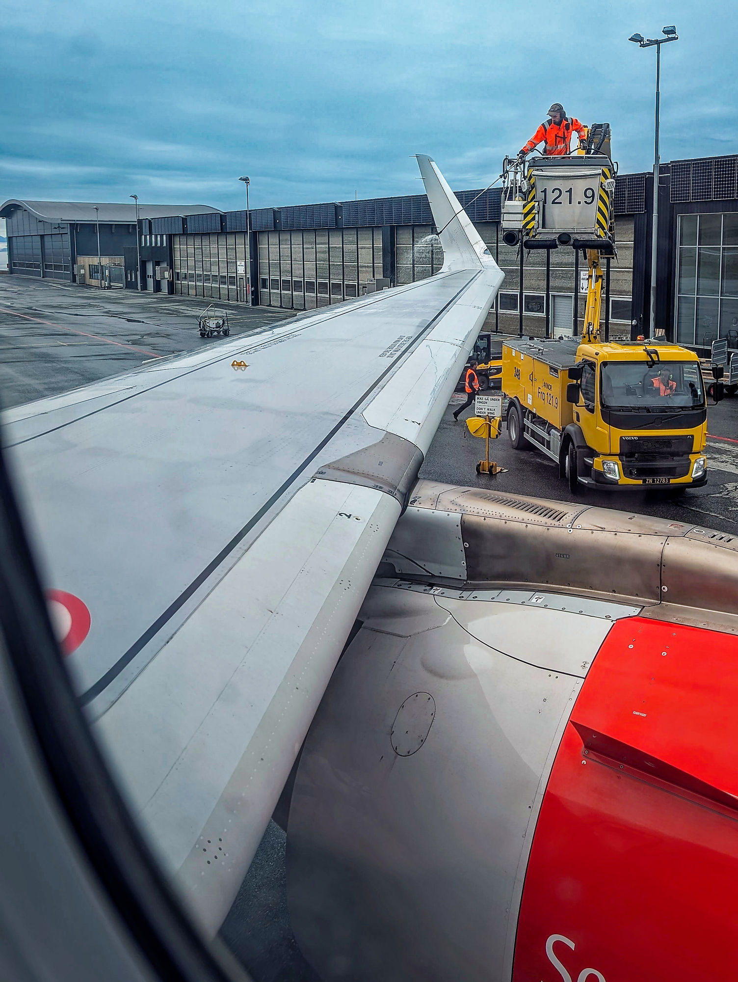 Flugzeugenteisung am Flughafen. Flugzeugflügel und gelber Enteisungswagen. Winterflugbetrieb.