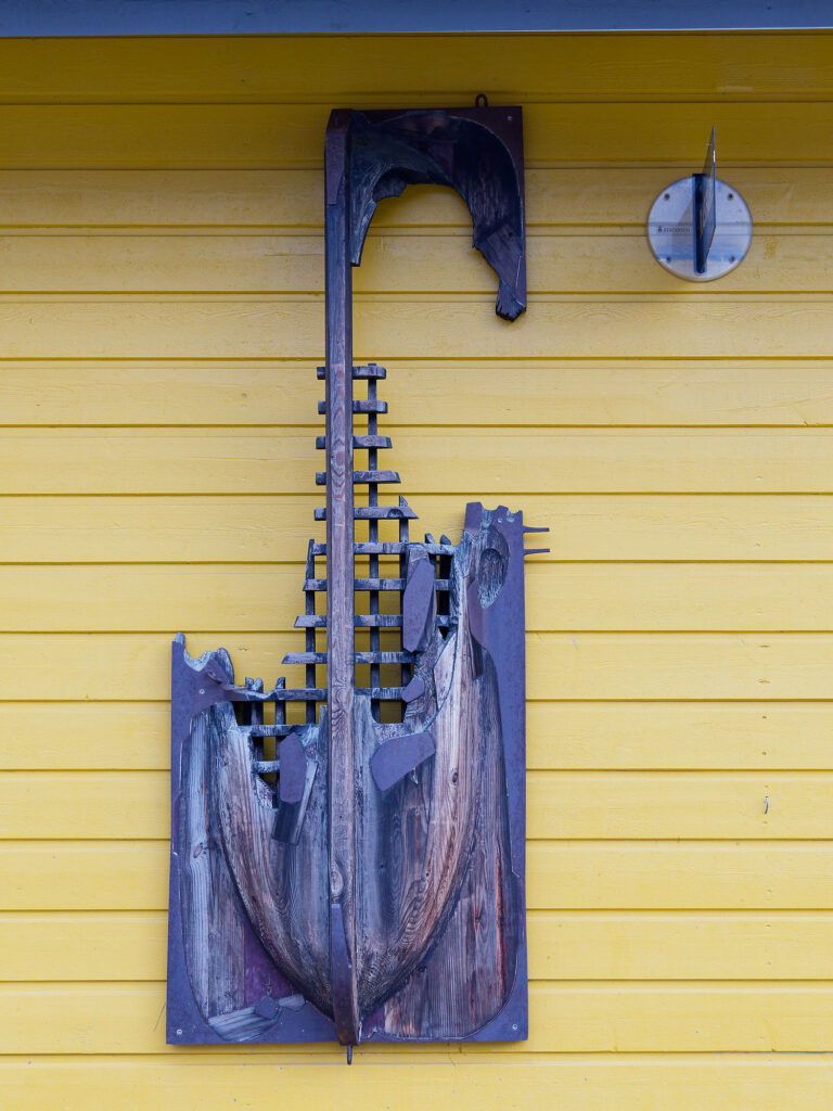 Gelbe Hauswand in Longyearbyen, Svalbard, mit dekorativer Holzschiff-Skulptur. Nordpolarregion Kunst.