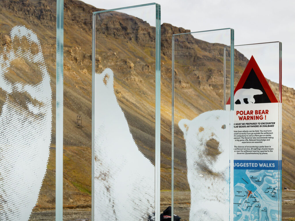 Longyearbyen, Svalbard: Eisbär-Warnschild. Glaspaneele mit Eisbär-Motiven vor Bergkulisse. Sicherheitshinweis.