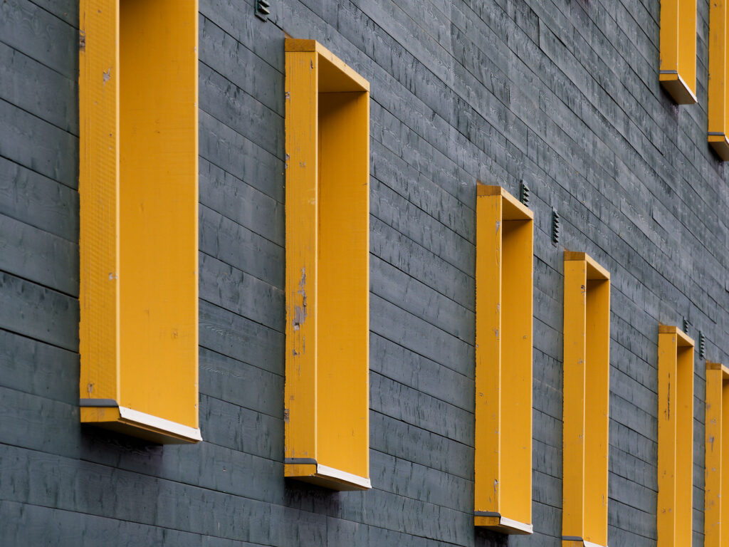 Fassade in Longyearbyen: Graue Holzverkleidung mit gelben, rechteckigen Akzenten. Architektur Detail.
