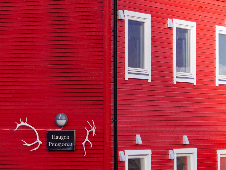 Rote Holzwand mit Fenstern und Haugen Pensjonat Schild in Longyearbyen, Spitzbergen.