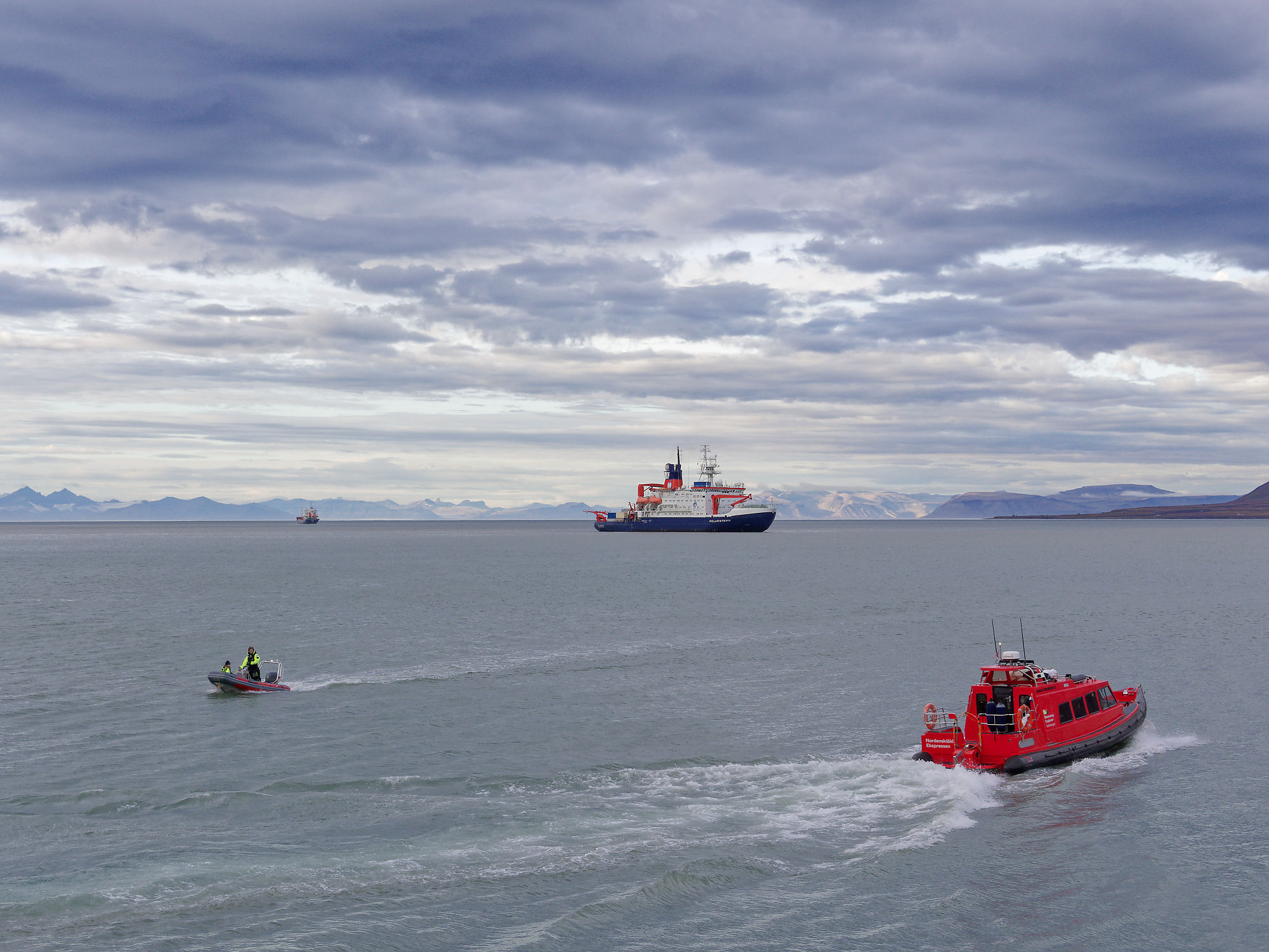Hafen Longyearbyen, Spitzbergen: Boote und Schiff auf dem Wasser unter bewölktem Himmel. Arktis-Kreuzfahrt.