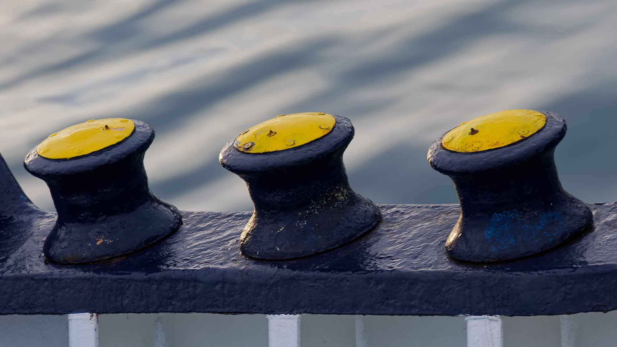 Drei Schiffsfender mit gelben Kappen auf blauem Geländer. Schifffahrt-Zubehör.