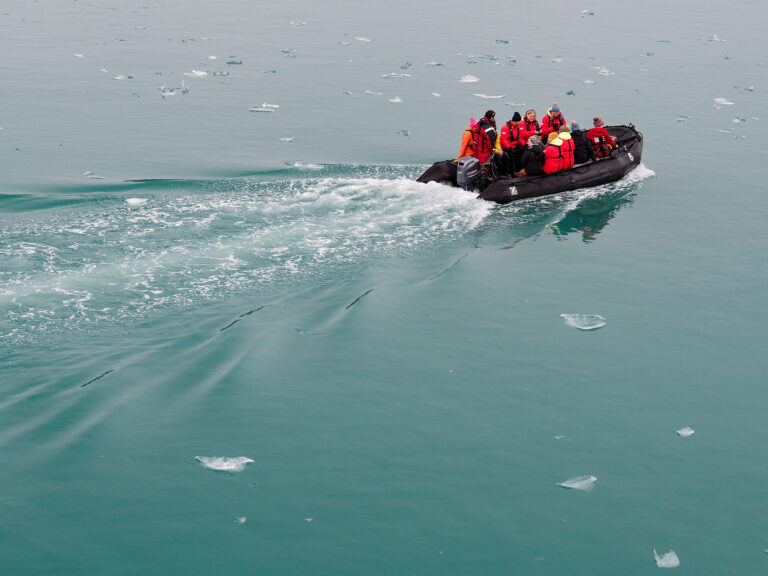 Schlauchboot-Tour im Magdalenefjord, Spitzbergen. Eisberge im Wasser. Reisegruppe mit roter Kleidung.