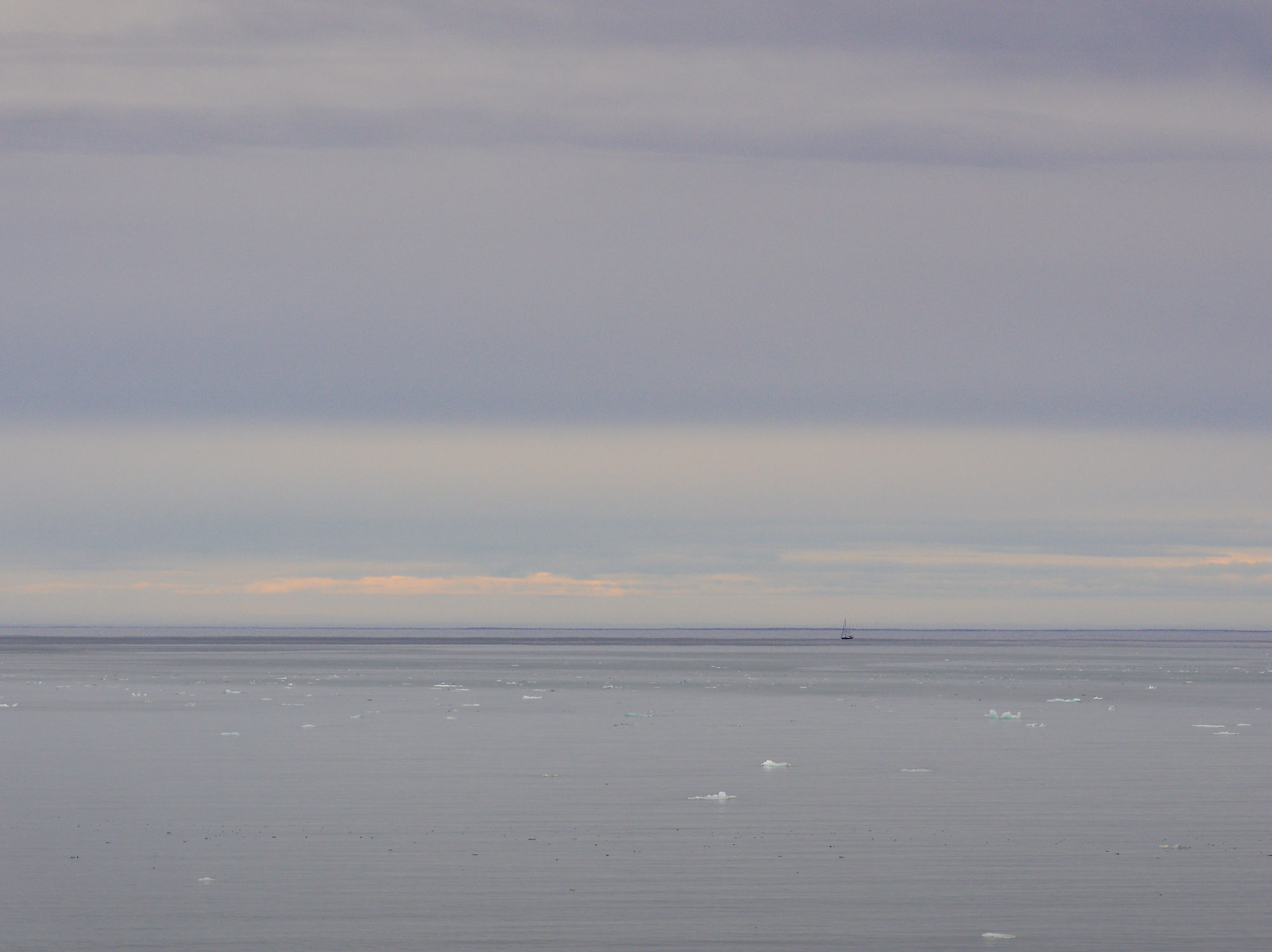 Magdalenefjord: Eisberge im Wasser, Segelboot am Horizont unter bewölktem Himmel.