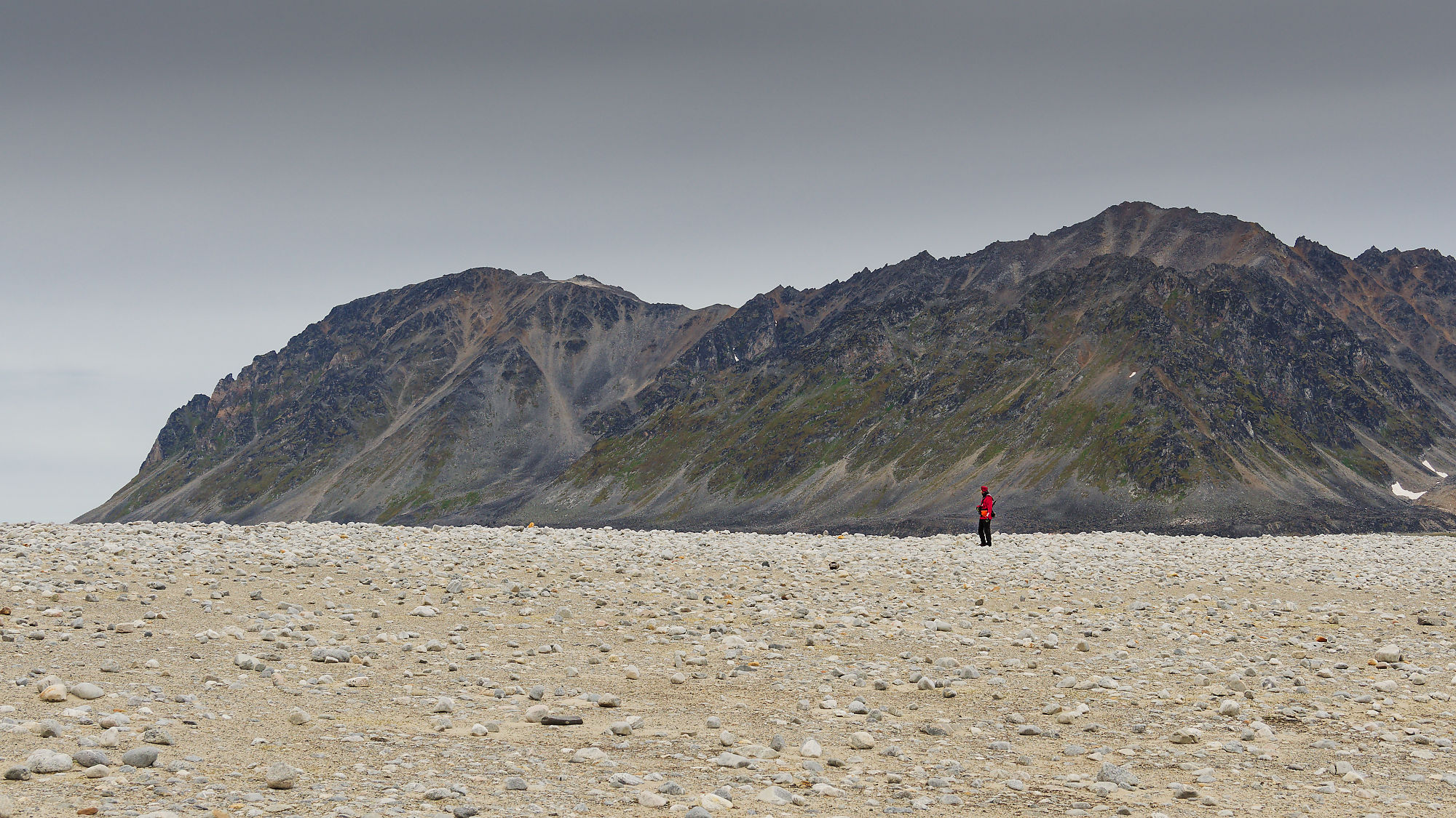 Magdalenefjord, Spitzbergen: Wanderer vor Bergkulisse. Arktis-Landschaft mit Felsen und Kiesstrand.
