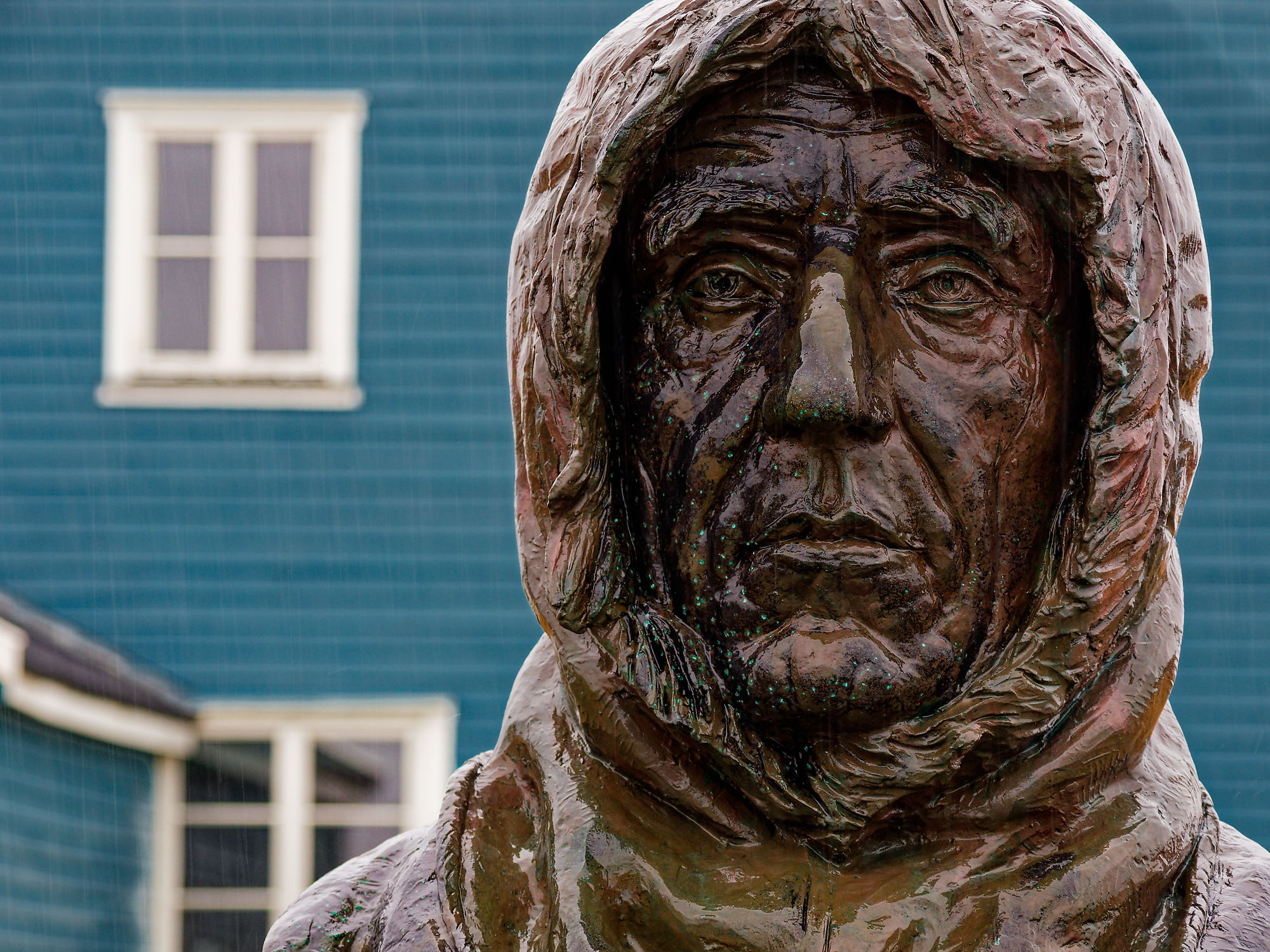 Bronzestatue von Roald Amundsen mit Kapuze in Ny-Ålesund, Spitzbergen. Blaue Gebäude im Hintergrund.