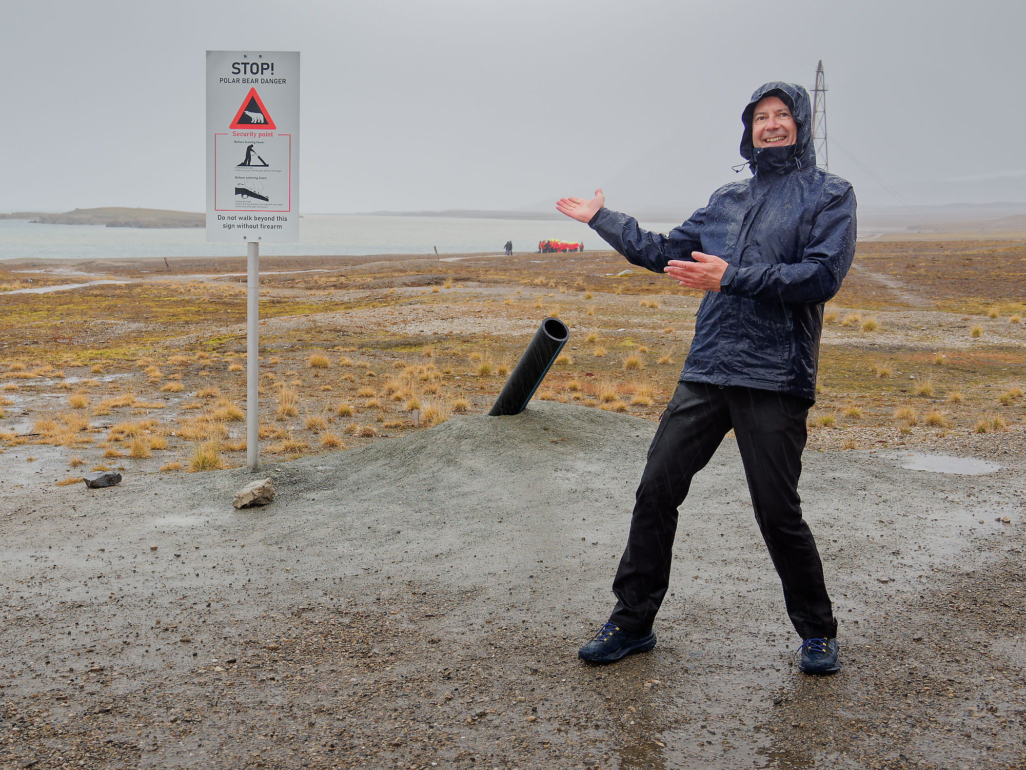 Ny-Ålesund, Svalbard: Mann zeigt auf Eisbär-Warnschild. Arktis-Reise, Polargebiet. Gefahr!