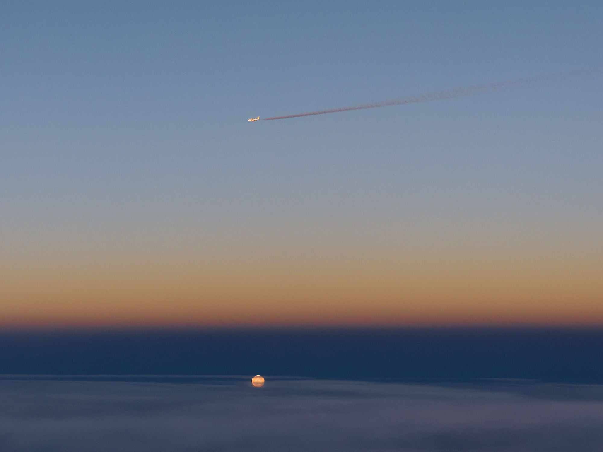 Flugzeug am Himmel mit Kondensstreifen, Mondaufgang über Wolken. Abendrot.