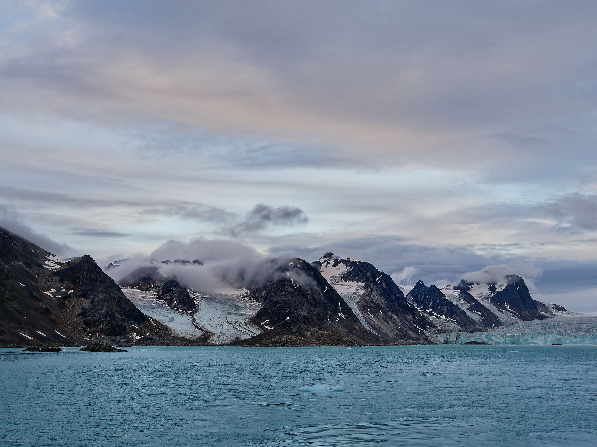 Smeerenburgfjorden, Spitzbergen: Arktische Landschaft mit Bergen, Gletscher und blauem Wasser unter bewölktem Himmel.